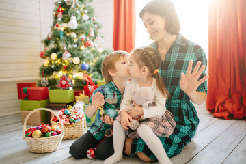 Happy family mom, son and daughter on a Christmas winter sunny morning in a decorated Christmas celebration room with a Xmas tree and gifts.