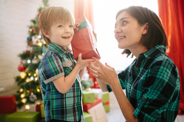 Happy family mom and son on a Christmas winter sunny morning in a decorated Christmas celebration room with a Xmas tree and gifts.