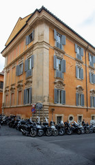 Fototapeta na wymiar Yellow facade of a building in Rome with lots of scooters parked on the street