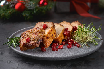 Sliced baked pork with tangerine sauce and herbs on a plate. Dark background