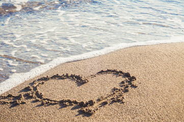 A drawing of a heart on asand at a beautiful sea background.