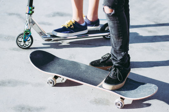 Close up of tennagers feet riding skateboard and scooter at hte skatepark. Trendy young skater enjoying outdoors in the city with kick scooter and skate board. Youth freedom sport and carefree concept