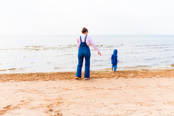 The child runs away into the sea. Woman with a child on the beach in front of open water.