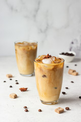 Cold brew coffee with spices and milk on light grey background. Spicy coffee with ice cubes.