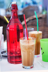 Greek coffee frappe in a glass with a straw on the table a bright red bottle of water
