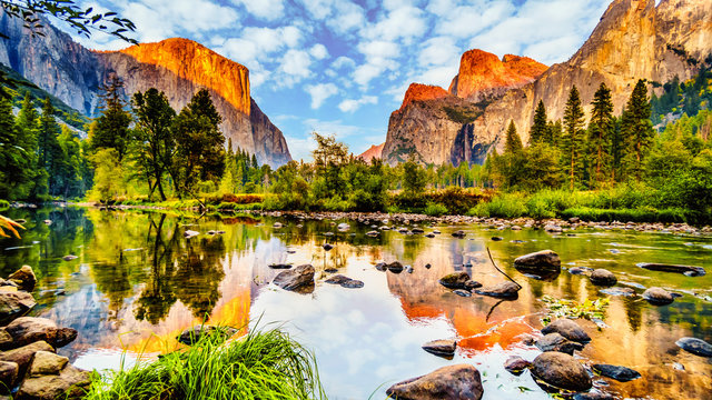 Sunset glow over El Capitan on the left and Cathedral Rocks, Sentinel Rock and Bridalveil Fall on the right and reflecting in the calm water of Merced River in Yosemite National Park, California, USA
