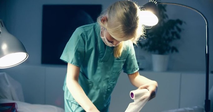 Cute little girl wearing doctor suit playing at home, pretending to be a surgeon, bandaging her teddy bear. Shot on RED Cinema camera with Cooke Prime lenses