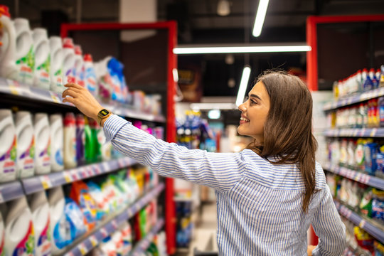 Young smiling woman groceries shopping in local supermarket. She always compares brands and prices. Beautiful caucasian woman shopping personal hygiene products at supermarket.