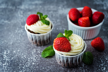 Chocolate cupcakes with cream cheese frosting, mint leaves and strawberries