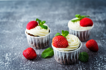 Chocolate cupcakes with cream cheese frosting, mint leaves and strawberries