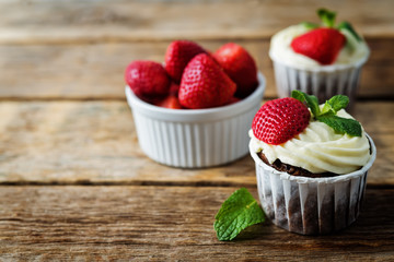 Chocolate cupcakes with cream cheese frosting, mint leaves and strawberries