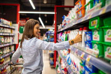 Casual woman choosing food from shelf in supermarket. Smiling customer standing near shelves. Beautiful young woman shopping in a grocery store/supermarket