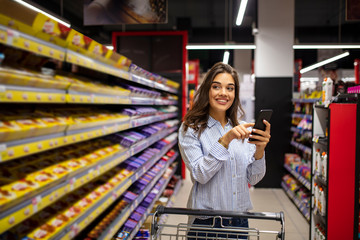 Woman do shopping check to buy list in phone. Women shopping in supermarket. Pretty young woman buying groceries in a supermarket/mall/grocery store.