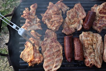 A barbecue where large pieces of meat and sausages are grilled.