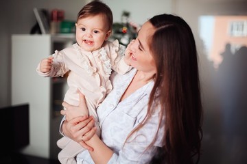 Happy beautiful woman having fun with her little daughter near the Christmas tree. Mom holds a cheerful baby in her arms
