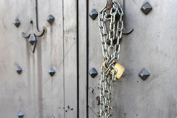 Closeup of old Iron door with closed padlock on a chain. A chain of silver color with closed padlock on an old gate.