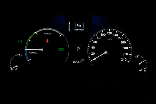 The dashboard of the car is glowing white with arrows at night with a speedometer, charge battery level and other tools to monitor the condition of the hybrid vehicle in modern style on black