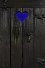 Kleine dunkle Holztür mit ausgeschnittenem Herz und verschiedenen Beschlägen