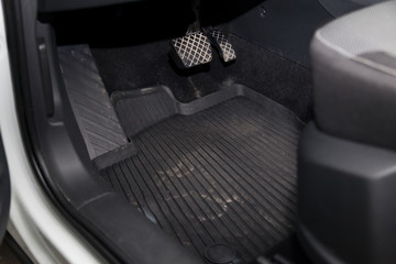 Dirty car floor mats of black rubber with gas pedals and brakes in the workshop for the detailing vehicle before dry cleaning. Auto service industry. Interior of sedan.