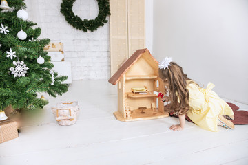 Baby Girl  playing with wooden doll house stuffed with mini furniture toys and doll. A funny little child in a yellow dress enjoys in the children's room