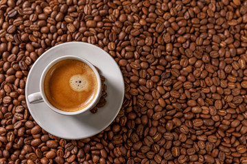 A small white cup of coffee stands on coffee beans. Fragrant pleasure. Background. Space for text. Top view.