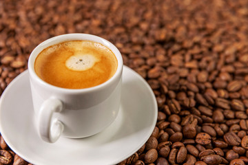 A small white cup of coffee stands on coffee beans. Fragrant pleasure. Background. Space for text. Close-up.