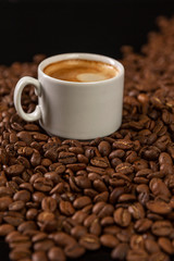 A small white cup of coffee stands on coffee beans. Fragrant pleasure. Background. Space for text. Vertical.
