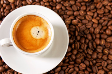 A small white cup of coffee stands on coffee beans. Fragrant pleasure. Background. Space for text. Close-up.