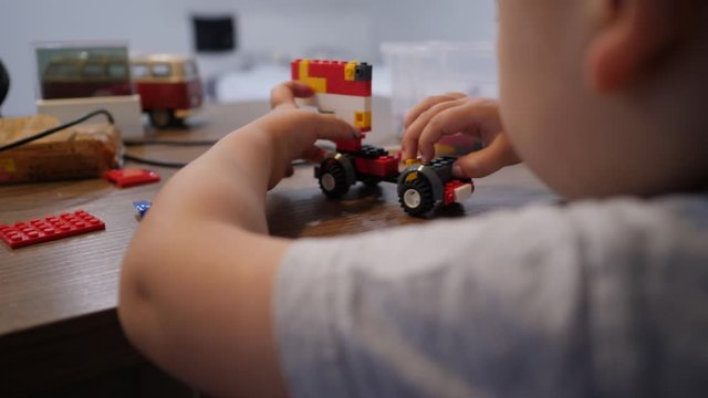 Baby boy play with toy car made of colorful plastic blocks. Closeup of hands
