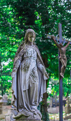 Statue of the grieving Virgin Mary against the background of the cross with the crucifixion of Jesus.