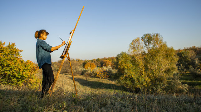 young woman artist drawing a picture on canvas, general view of the landscape and the artist with an easel, a concept of art, hobby