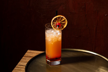 Tequila Sunrise, a cocktail with real orange juice., tequila, grenadine, garnished with candy cherry and charred orange