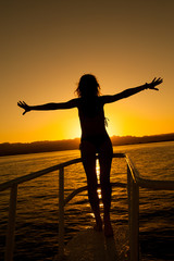 Fototapeta premium Woman silhouette posing against the sun on a sunset in the sea