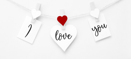 I löve you - Clothes pegs  with red wooden hearts and paper notes hang on rope isolated on white texture background, with space for text