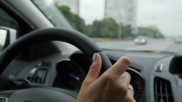 Female hands on a steering wheel. Woman tap the rythm with fingers while driving