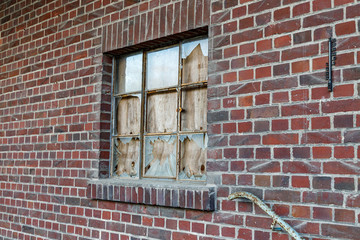 Rote Backsteinwand mit Fenster kaputtes Glas verschlossen mit einem Holz Brettals Hintergrund oder Textur
