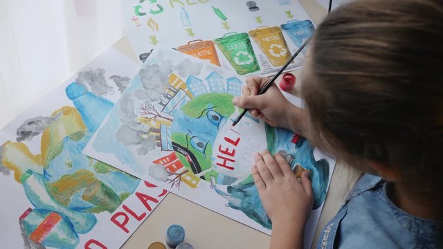 Top view of a schoolgirl paints posters calling to save planet Earth from pollution
