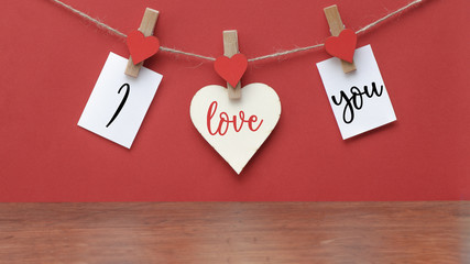 I love you - Clothes pegs with wooden hearts and paper notes hang on rope isolated on red texture...
