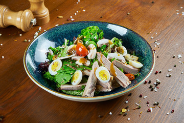 Tasty, fresh Salad with duck breast, spinach, quinoa, quail eggs and cherry tomatoes in a blue bowl on a wooden background. Healthy Fitness Nutrition. Close up food