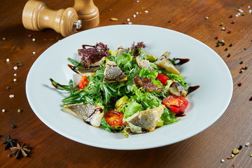 Gourmet salad served with roasted sea bass, spinach, lettuce, cherry tomatoes on a wooden background. Delicious seafood salad. Healthy food. Diet and fitness nutrition