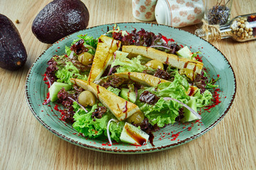 Tasty salad with tofu, avocado and olives lettuce in a white bowl on a wooden background. Vegetarian food. Tasty and wholesome food