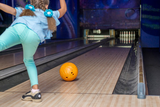 Young Girl Throwing A Ball In Bowling Club. Kid Is Playing Bowling. View From Behind