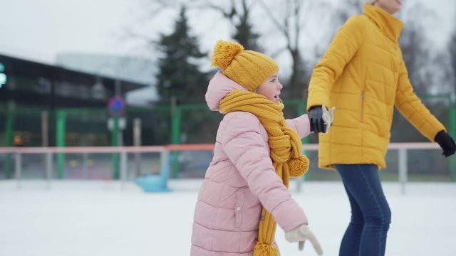 Tilt up tracking shot of mother and little daughter ice skating in slow motion holding hands into loving fathers embrace at outdoor ice rink