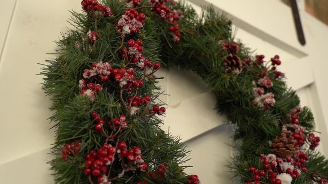 Closeup view of green holiday decorative Christmas green wreath decorated with red decorative berries and snow hanging on wooden door. Real time full hd video footage.