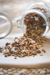 Glass jar up to the top filled with organic granola with nuts and coconut. Jar with granola on a background of baking paper. Healthy lifestyle concept.