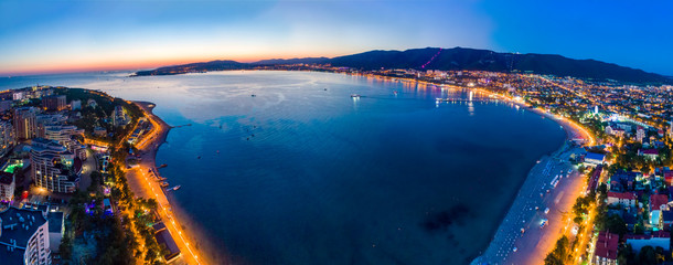 Evening panorama of the seaside resort of Gelendzhik. the sun went down, dark blue sky and sea. Visible Bay, beach and promenade in the lights.  The silhouettes of the mountains