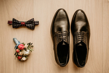 Close up of modern groom accessories. Black bowtie, leather shoes and flower boutonniere on rustic background. Set for formal style of wearing isolated on white background
