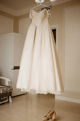 Fototapeta na wymiar Wedding dress on hanger and shoes on the floor in the bride room. On her wedding day
