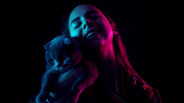 pets and people concept - happy young woman with cat in neon lihgt