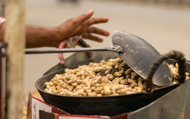peanuts are roasting using dry sand on a big pan with a big spoon in road side